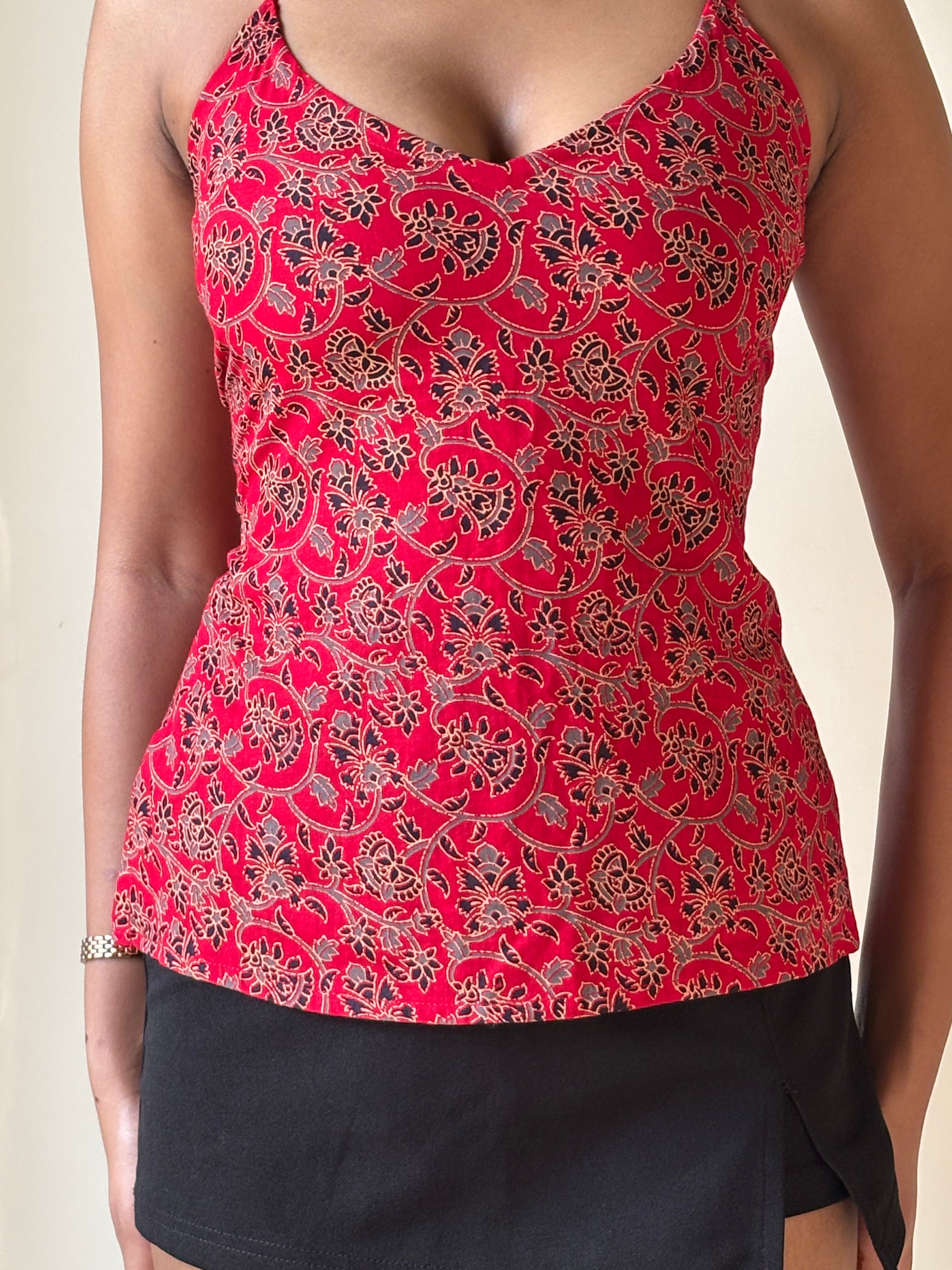 Red patterned top worn by a person on a beige background. A woman modeling a red and white printed, backless, knot-back top with blue jeans, alongside product details including the name 'Rakt - Red Backless Knot-Back Printed Top'.