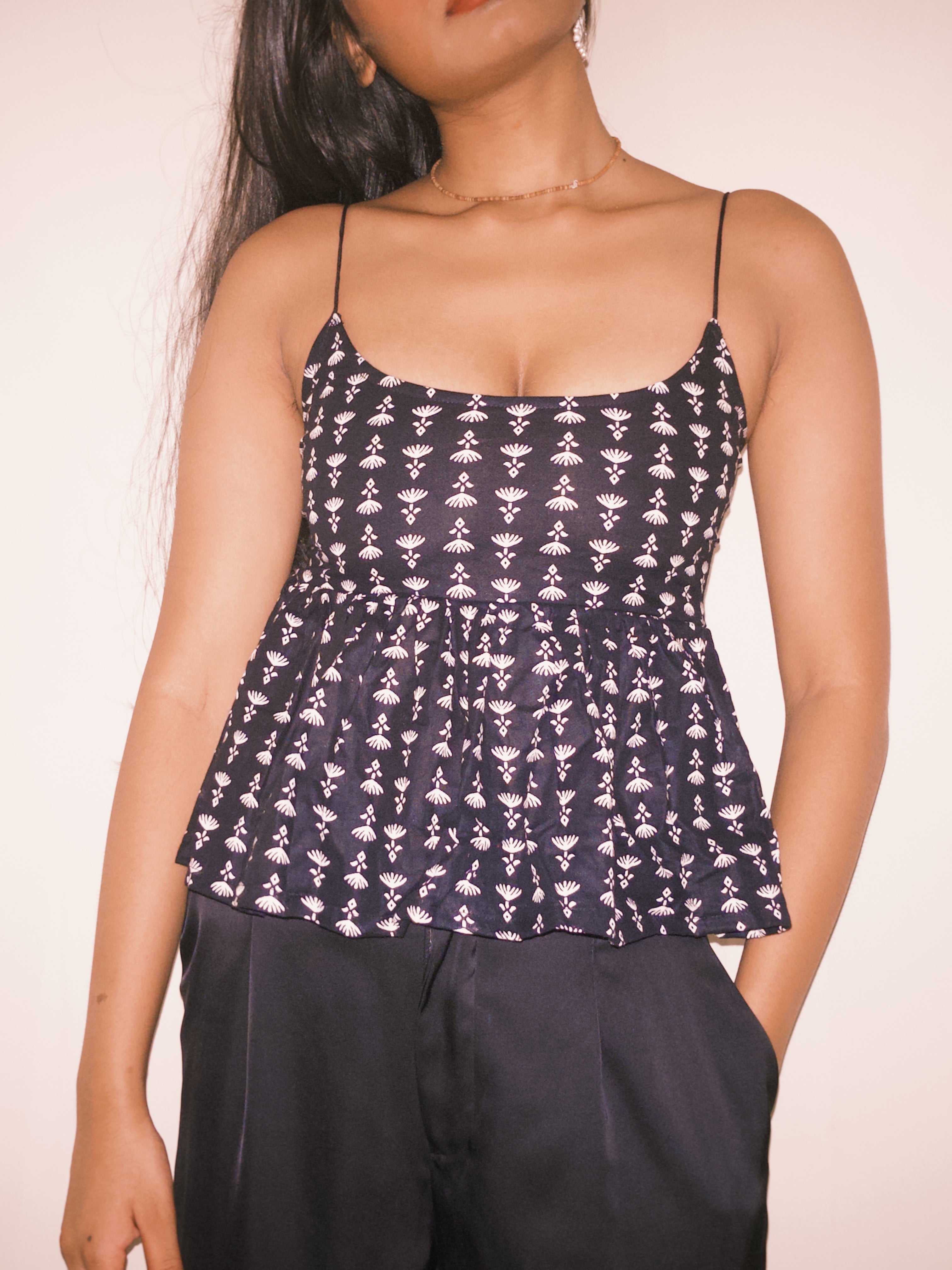 Person wearing a black and white patterned top with a plain  This is a dark-colored backless top with a white pattern and a criss-cross lace-up back detail.