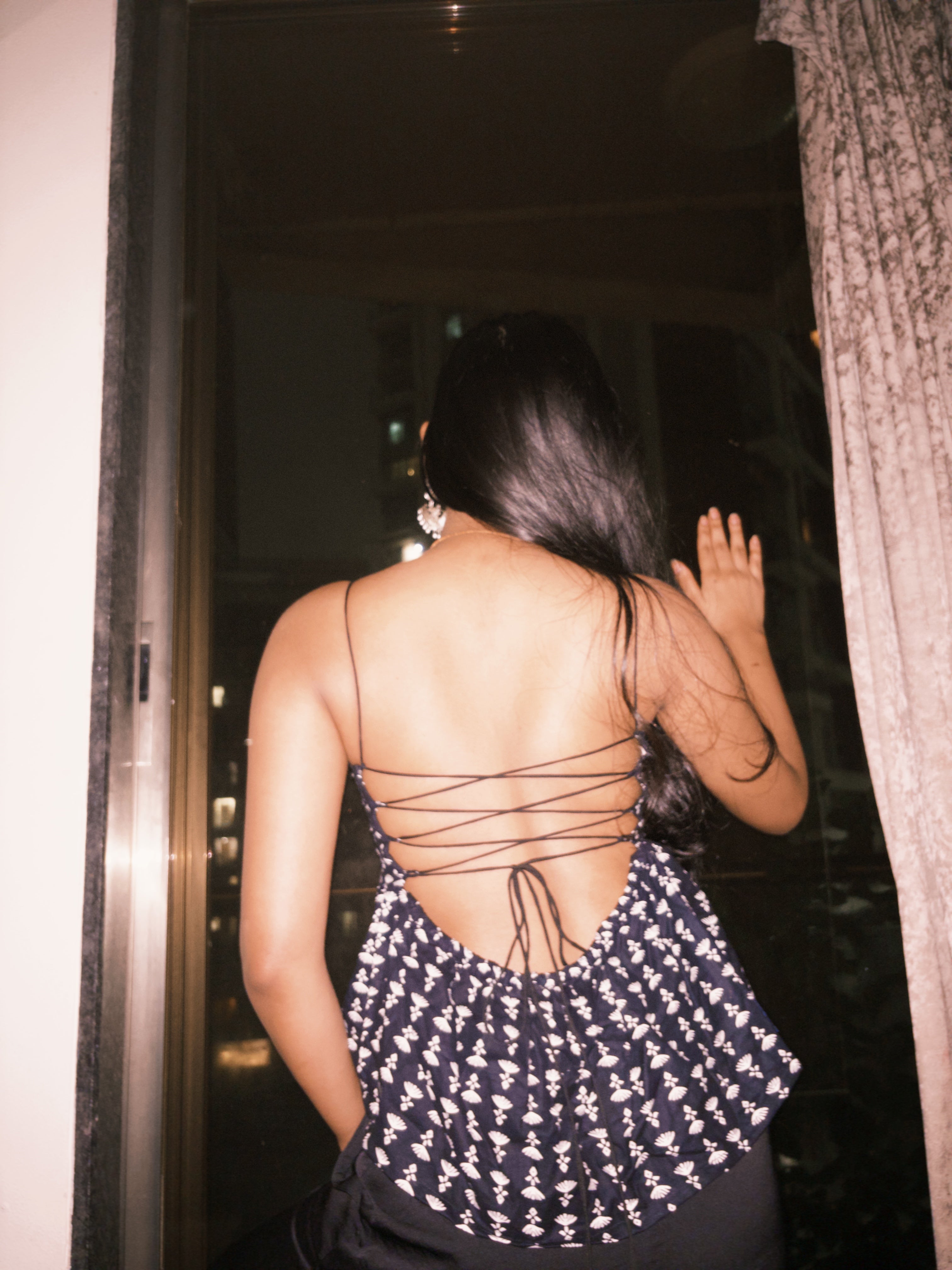 Woman wearing a black and white patterned dress with lace-up back. This is a dark-colored backless top with a white pattern and a criss-cross lace-up back detail.