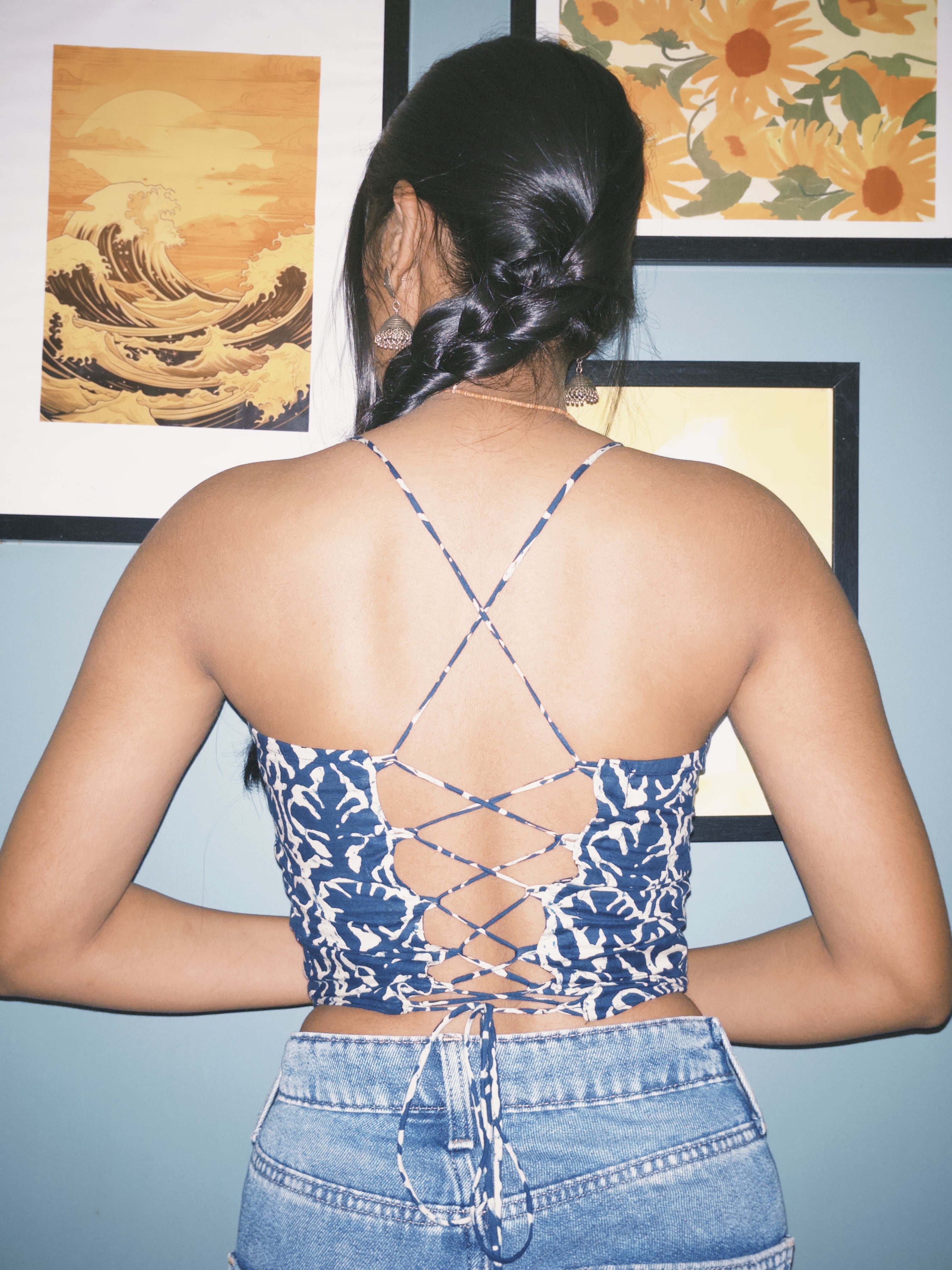 Person wearing a blue floral crop top with criss-cross back design, standing in front of framed artwork. Surzaa backless blue and white patterned crop top with a lace-up back. 